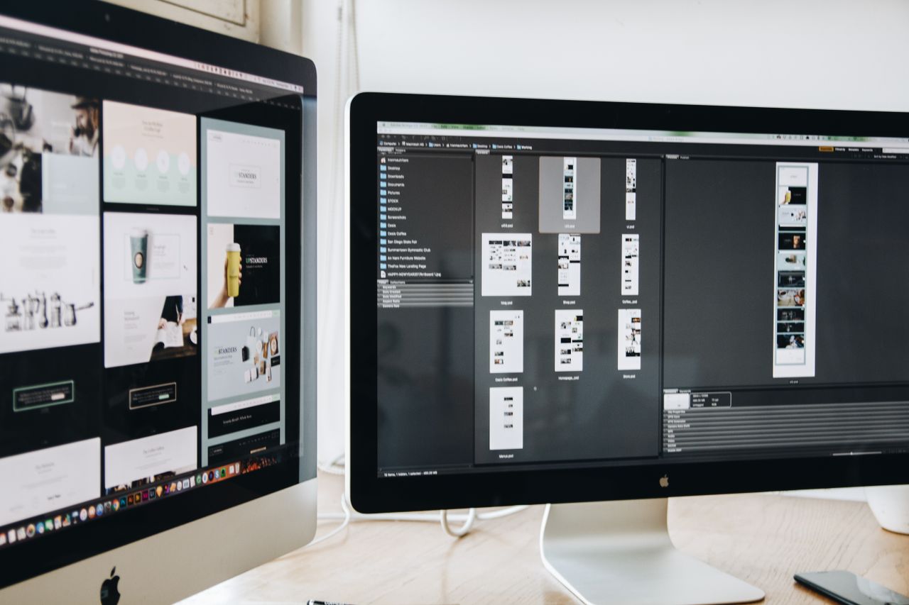 Moderní pracovní prostor s dvojicí počítačových monitorů zobrazujících webdesignové projekty, který zdůrazňuje technologie a produktivitu.